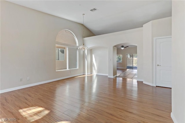 empty room with hardwood / wood-style flooring, vaulted ceiling, and ceiling fan with notable chandelier