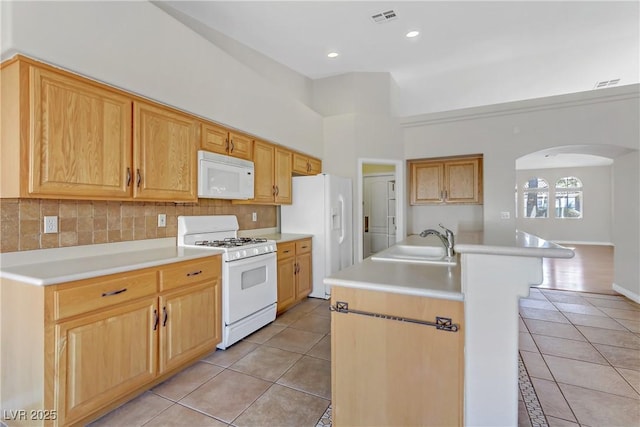 kitchen featuring sink, light tile patterned floors, white appliances, a kitchen island with sink, and decorative backsplash