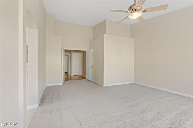 spare room with a high ceiling, light colored carpet, and ceiling fan