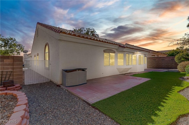 back house at dusk featuring a patio area and a lawn