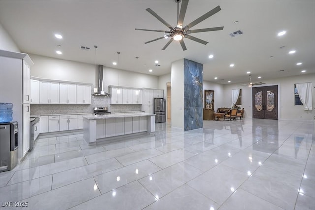 kitchen with white cabinetry, a center island, pendant lighting, stainless steel appliances, and wall chimney range hood