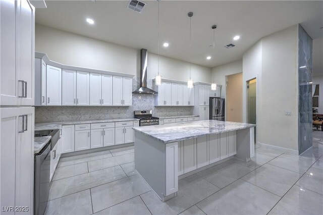 kitchen featuring appliances with stainless steel finishes, decorative light fixtures, white cabinets, a center island, and wall chimney exhaust hood