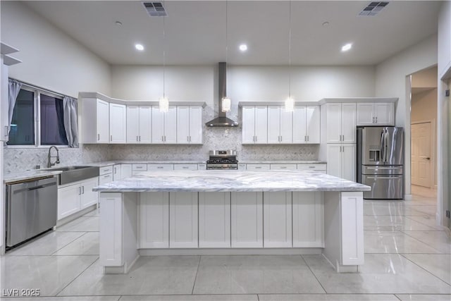 kitchen with decorative light fixtures, a center island, wall chimney exhaust hood, and appliances with stainless steel finishes