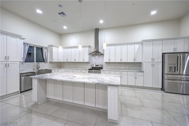 kitchen with white cabinetry, hanging light fixtures, light stone counters, stainless steel appliances, and wall chimney exhaust hood