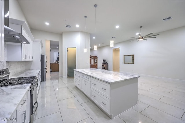 kitchen with wall chimney range hood, stainless steel appliances, light stone counters, white cabinets, and a kitchen island