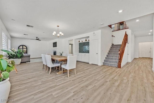 dining area with ceiling fan with notable chandelier and light hardwood / wood-style floors