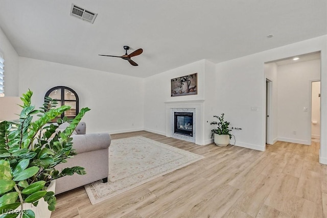 living room with a fireplace, ceiling fan, and light wood-type flooring