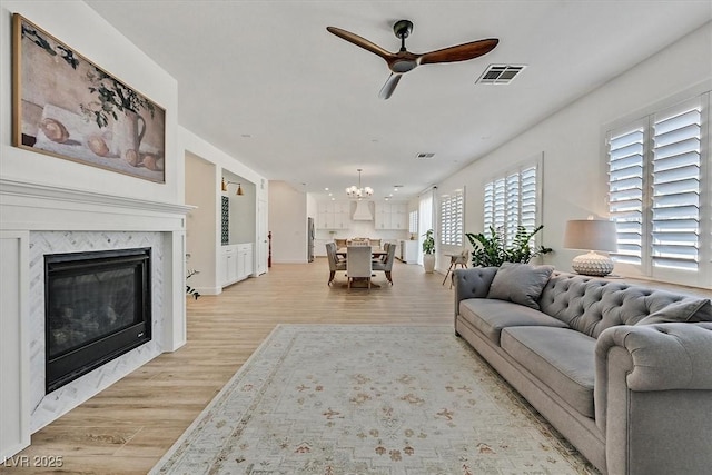 living room with a fireplace, ceiling fan with notable chandelier, and light hardwood / wood-style flooring