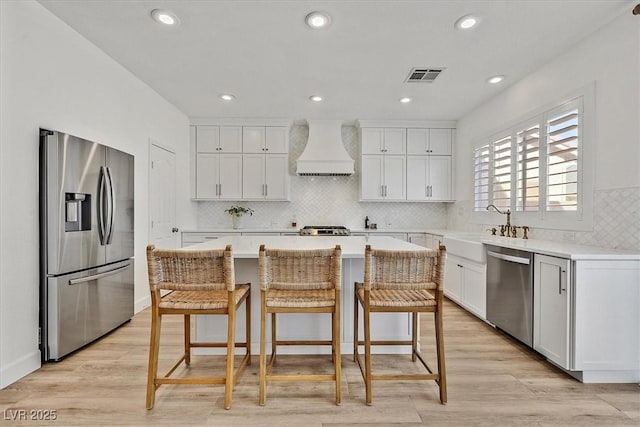 kitchen featuring white cabinetry, stainless steel appliances, custom range hood, and a kitchen island