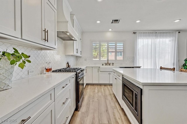 kitchen with stainless steel microwave, white cabinetry, sink, gas stove, and custom range hood