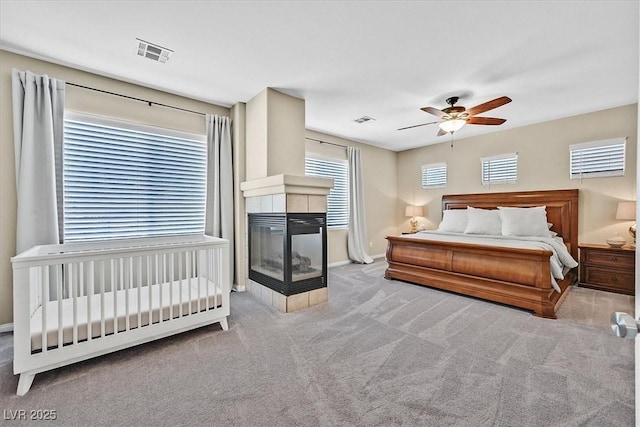 bedroom with a tiled fireplace, light colored carpet, and ceiling fan