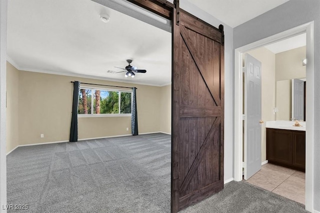 empty room with ornamental molding, light colored carpet, a barn door, and ceiling fan