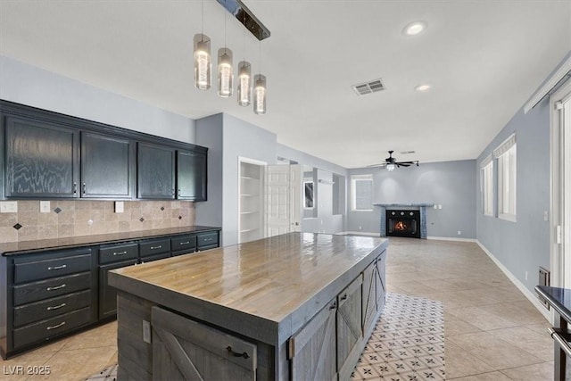 kitchen with pendant lighting, ceiling fan, butcher block counters, a center island, and tasteful backsplash