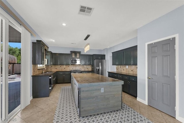 kitchen with sink, hanging light fixtures, light tile patterned floors, a kitchen island, and stainless steel appliances