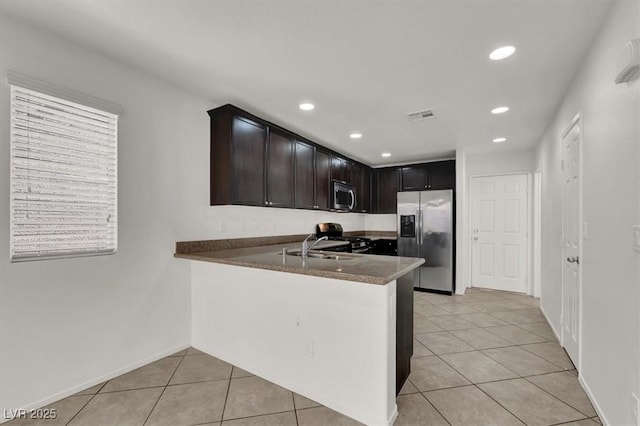 kitchen featuring dark stone countertops, stainless steel appliances, dark brown cabinetry, light tile patterned flooring, and kitchen peninsula