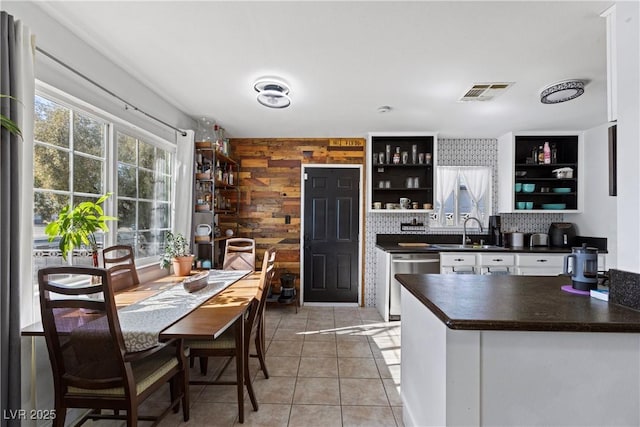 kitchen with light tile patterned flooring, wood walls, white cabinetry, dishwasher, and sink