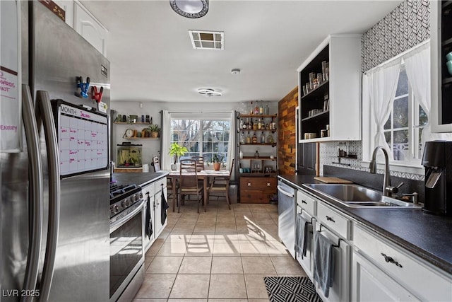 kitchen featuring sink, white cabinets, decorative backsplash, light tile patterned floors, and stainless steel appliances