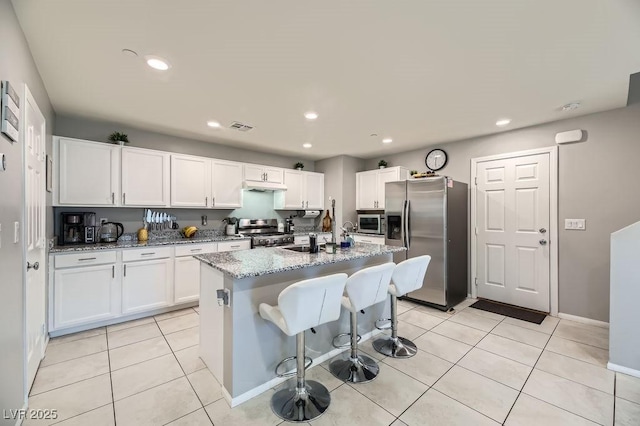 kitchen featuring appliances with stainless steel finishes, light stone countertops, an island with sink, and white cabinets