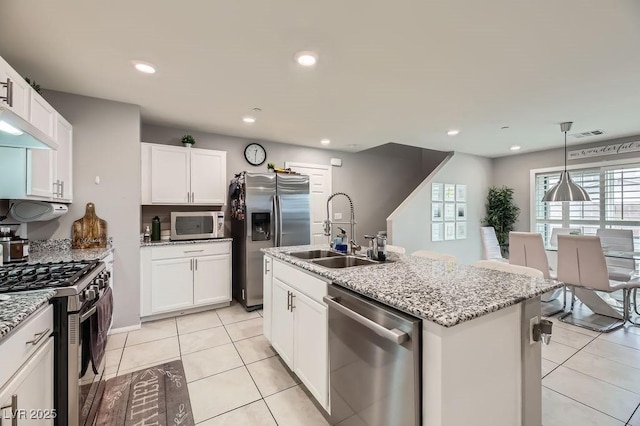 kitchen featuring pendant lighting, appliances with stainless steel finishes, a kitchen island with sink, light stone countertops, and white cabinets