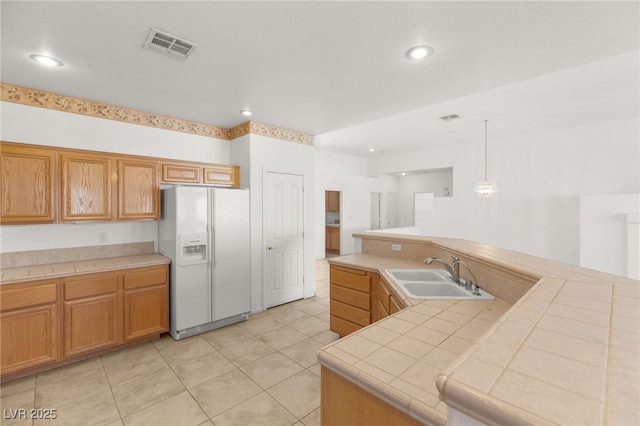 kitchen with pendant lighting, sink, white refrigerator with ice dispenser, tile counters, and light tile patterned floors