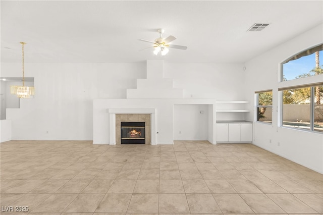 unfurnished living room with a tiled fireplace and ceiling fan with notable chandelier