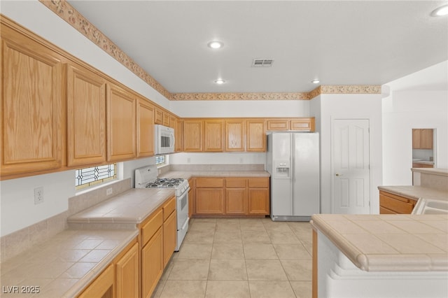 kitchen with white appliances, tile counters, and light tile patterned flooring