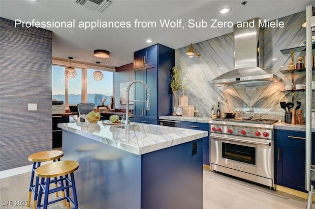 kitchen featuring premium range, ventilation hood, an island with sink, blue cabinets, and decorative light fixtures