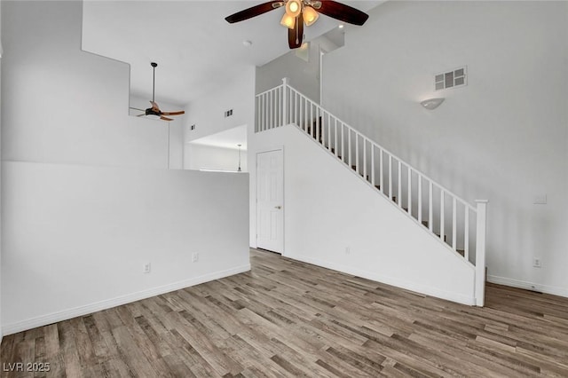 unfurnished living room with hardwood / wood-style flooring, ceiling fan, and a high ceiling