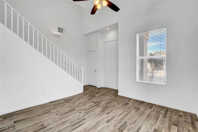 unfurnished living room with ceiling fan, light hardwood / wood-style floors, and a towering ceiling