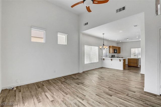 unfurnished living room featuring ceiling fan with notable chandelier and light hardwood / wood-style floors