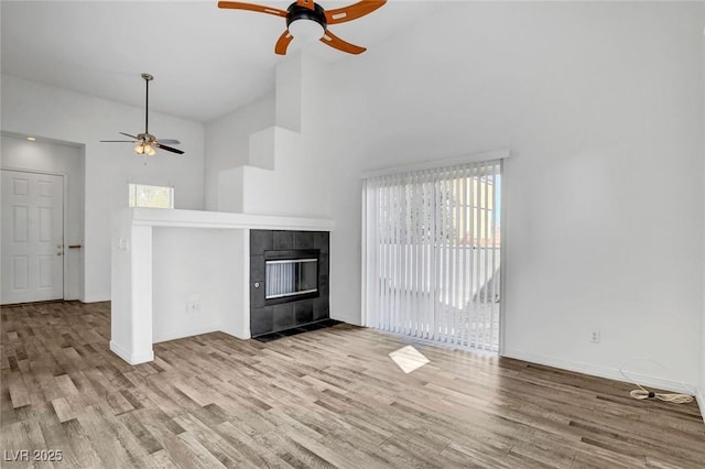 unfurnished living room with ceiling fan, high vaulted ceiling, light hardwood / wood-style floors, and a tile fireplace