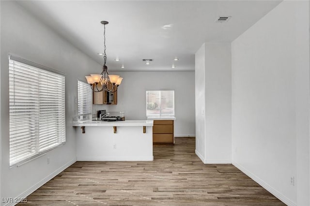 kitchen featuring sink, light hardwood / wood-style flooring, a notable chandelier, a kitchen bar, and kitchen peninsula