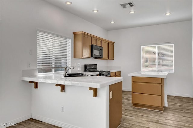 kitchen with sink, light hardwood / wood-style flooring, a kitchen breakfast bar, kitchen peninsula, and black appliances