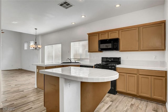 kitchen with sink, a center island, light wood-type flooring, pendant lighting, and black appliances