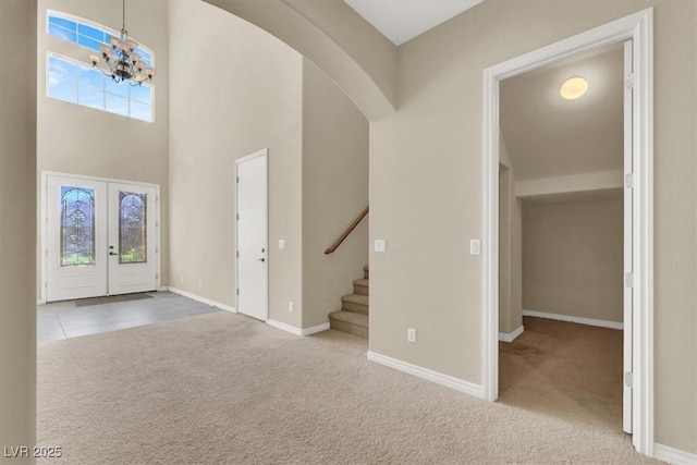 entrance foyer with a high ceiling, light carpet, a chandelier, and french doors