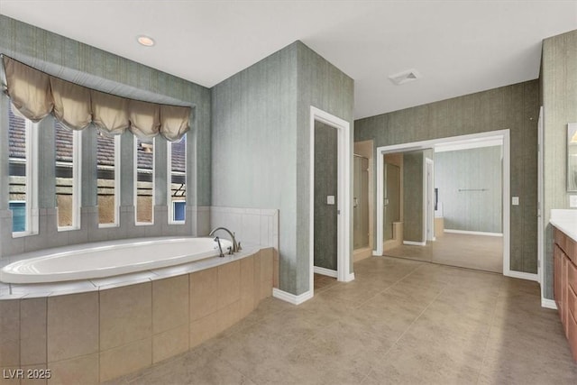 bathroom featuring a relaxing tiled tub, vanity, and tile patterned flooring