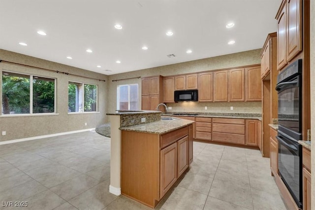 kitchen with light stone counters, light tile patterned floors, a kitchen island with sink, decorative backsplash, and black appliances