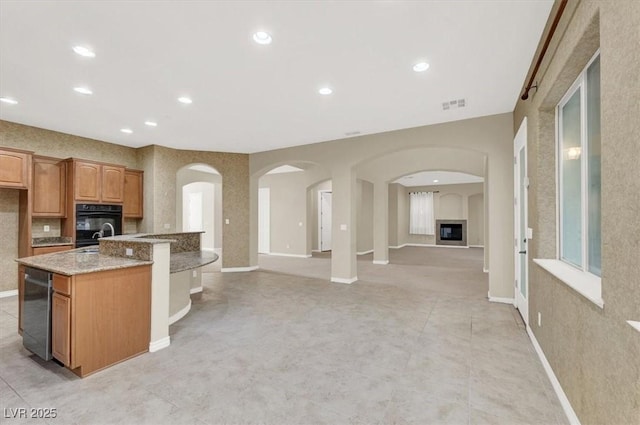 kitchen with light stone counters, beverage cooler, sink, and a center island with sink