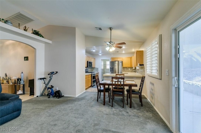 dining space with ceiling fan, light colored carpet, and vaulted ceiling