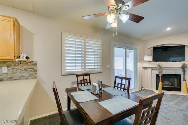 carpeted dining space with a tile fireplace and ceiling fan