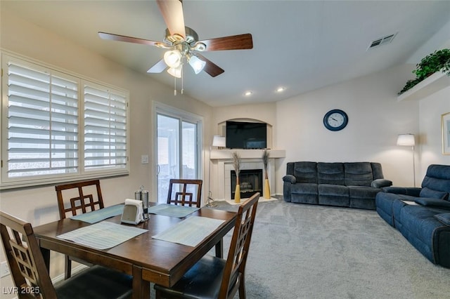 dining room with light carpet, a fireplace, and ceiling fan