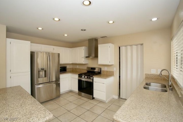 kitchen with wall chimney range hood, light tile patterned floors, sink, appliances with stainless steel finishes, and white cabinetry