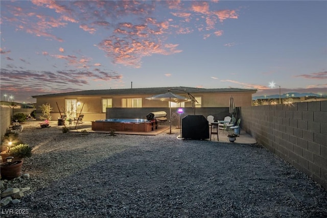 back house at dusk with a patio area and a hot tub