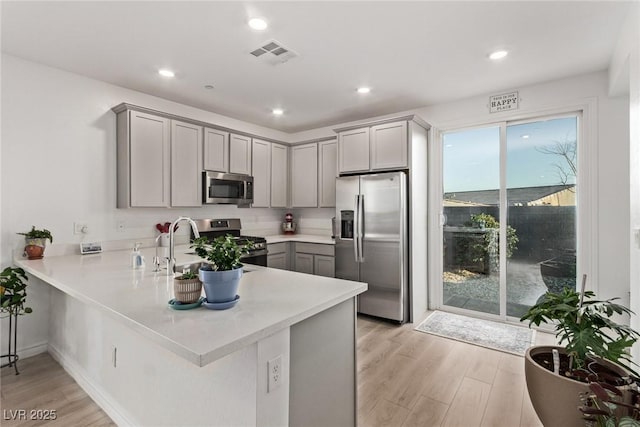 kitchen with gray cabinets, appliances with stainless steel finishes, light hardwood / wood-style flooring, and kitchen peninsula