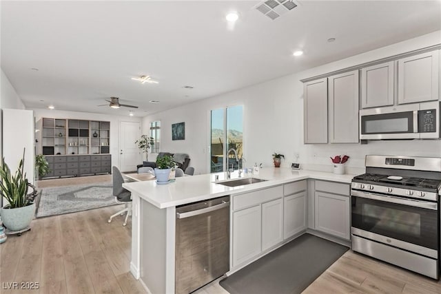 kitchen featuring sink, light wood-type flooring, kitchen peninsula, and appliances with stainless steel finishes