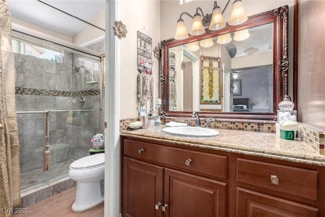 bathroom featuring vanity, toilet, a shower with door, and decorative backsplash