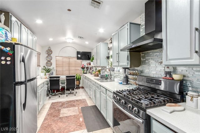 kitchen featuring vaulted ceiling, sink, backsplash, stainless steel appliances, and wall chimney range hood