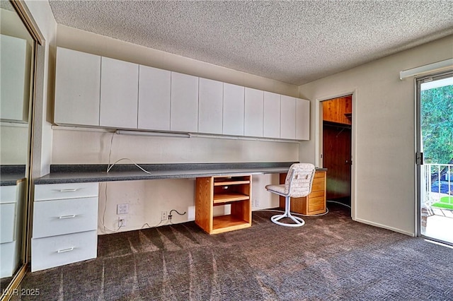 kitchen featuring white cabinetry, dark carpet, built in desk, and a textured ceiling