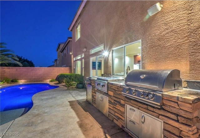 patio at twilight with a fenced in pool, an outdoor kitchen, and grilling area