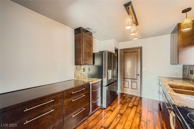 kitchen featuring appliances with stainless steel finishes, pendant lighting, wood-type flooring, backsplash, and light stone counters